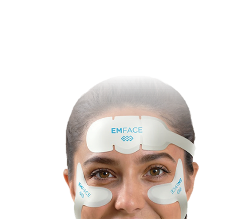 Close-up of a woman wearing white EMFACE facial devices on her forehead and cheeks against a black background, conveying a clinical, futuristic tone.
