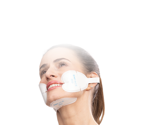 A woman with a serene smile wears a white face lifting mask that covers her chin and cheeks against a black background, suggesting skincare rejuvenation.